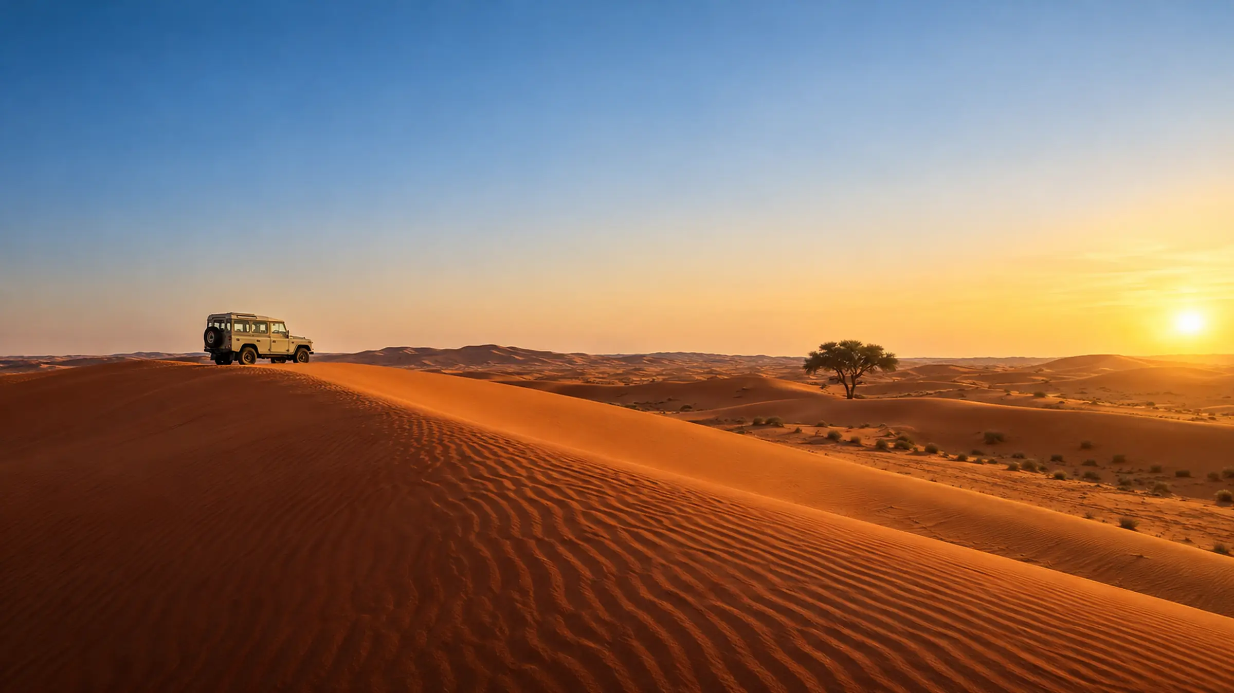 A restored Land Rover on a red dune ridge at sunset, a lone ghaf tree on the horizon